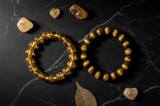 Two handcrafted energy bracelets, one clear yellow quartz and one tiger eye, on black marble.
