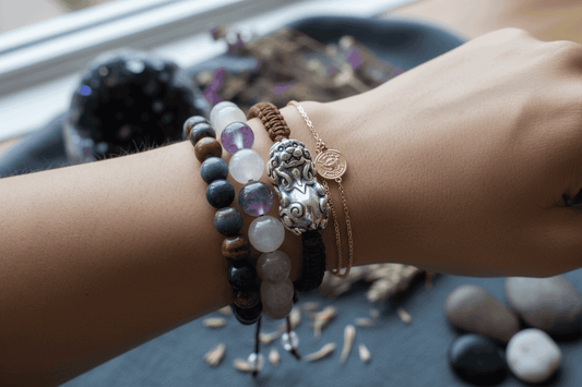 Hand wearing a set of handcrafted energy bracelets with crystals and a silver charm.