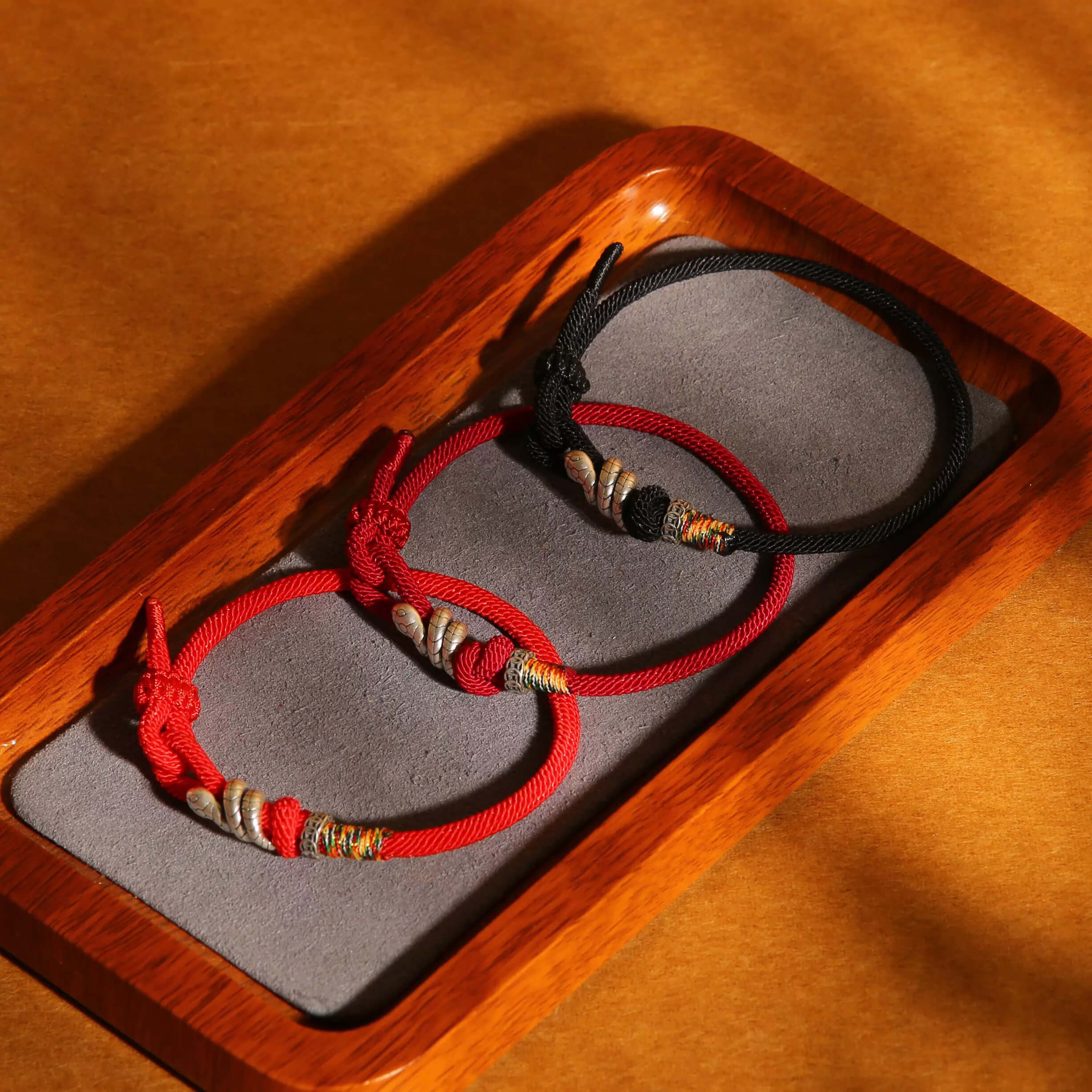 Three handcrafted energy bracelets in red and black on a grey display pad in a wooden tray.