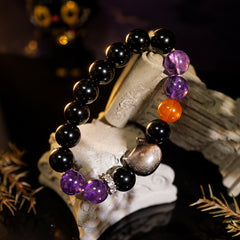 Side view of an amethyst and black obsidian bracelet with a carved cat centerpiece