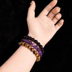 Three stacked gemstone bracelets in black, purple and golden brown worn on a wrist