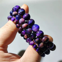 Starry Night Purple Tiger Eye Bracelet with constellation charms on dark blue cord, glowing under starry backdrop. Ideal for meditation and energy alignment.